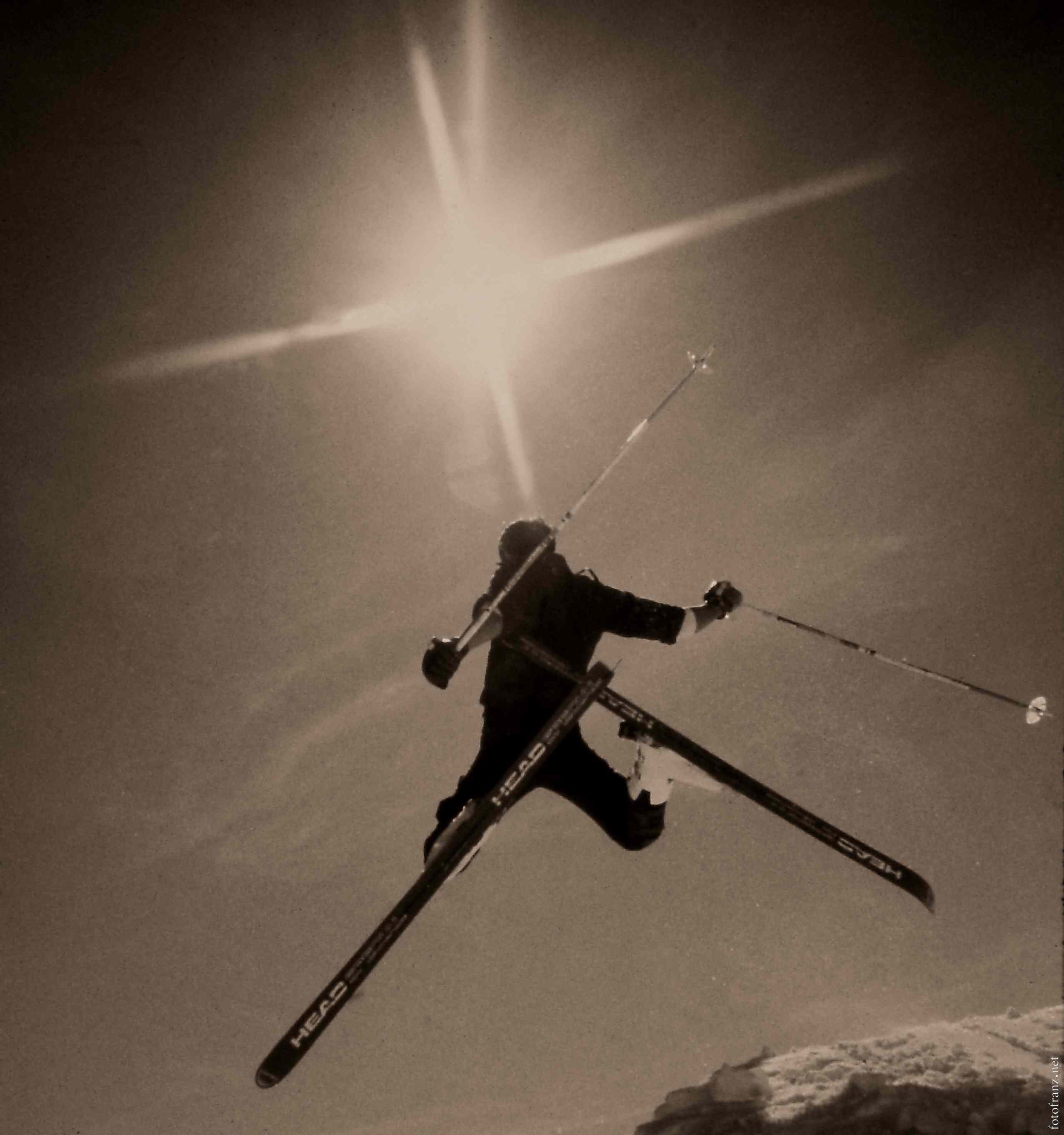 Ein Skifahrer springt in der Nacht auf Schnee, mit einem Sternenhimmel im Hintergrund.