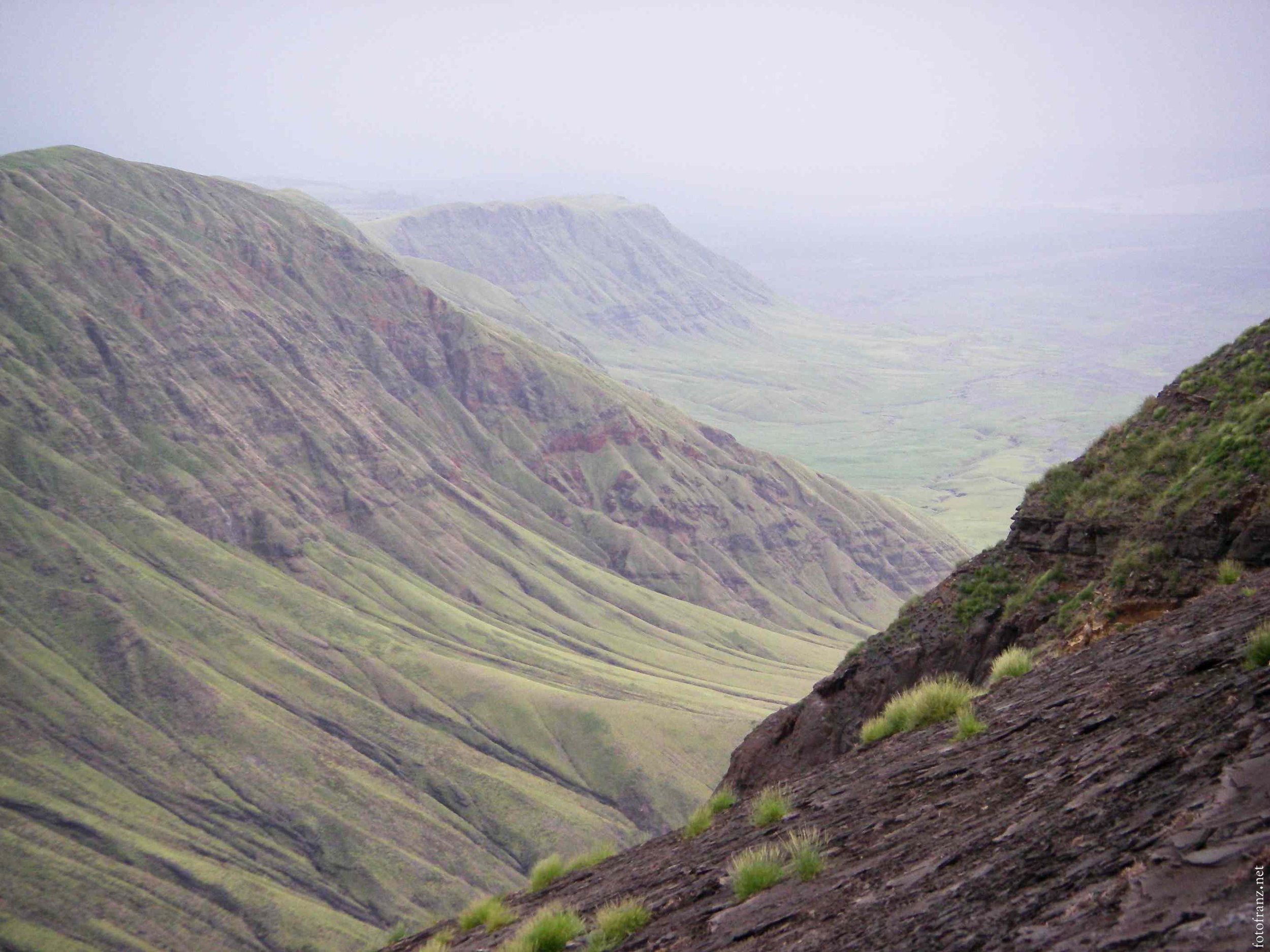 Eine bergige Landschaft mit grünen Hügeln und Felsen, die von Wolken umgeben ist.