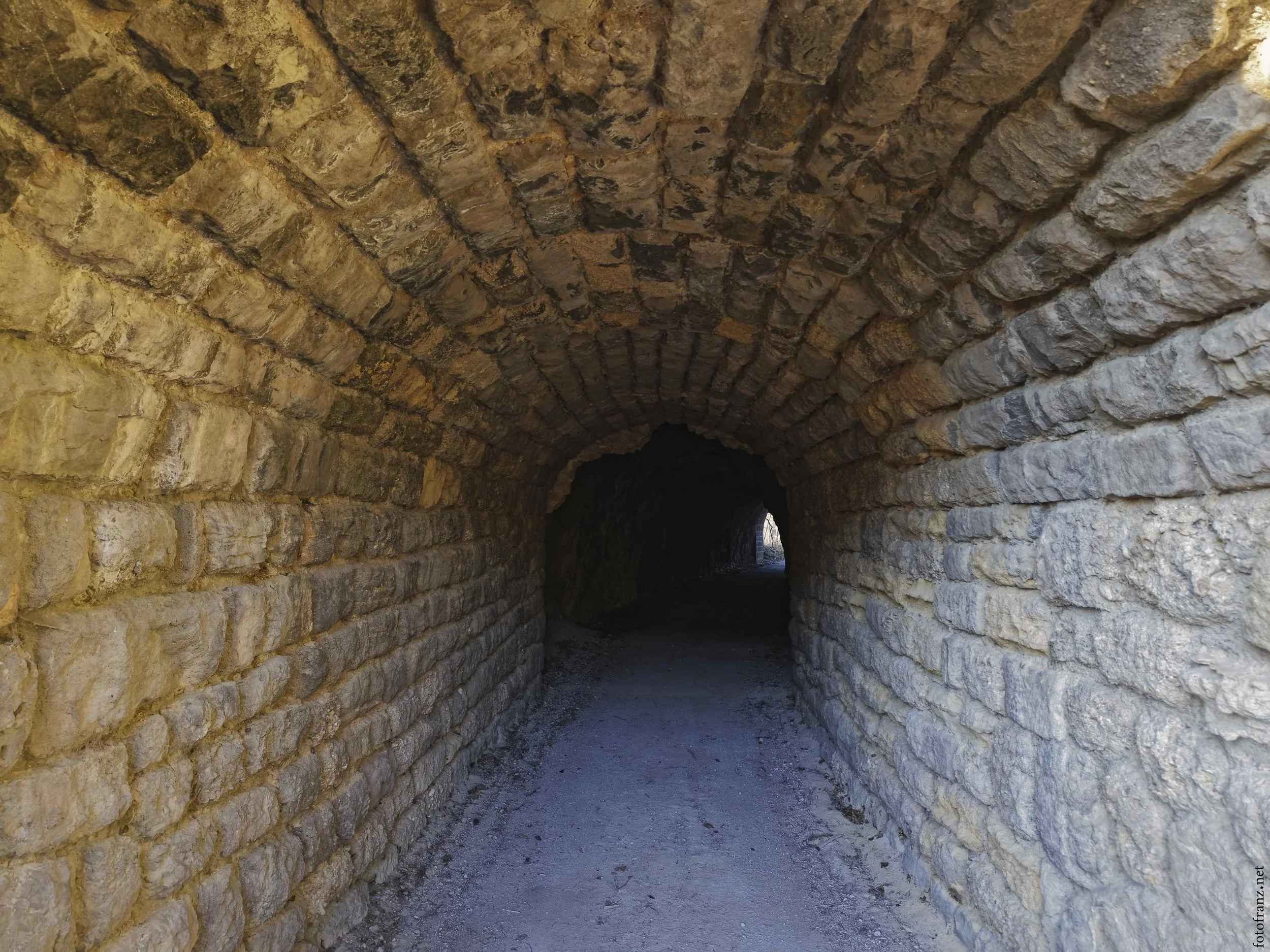 Ein Tunnel aus Ziegelsteinen mit Bögen, der ins Dunkle führt.