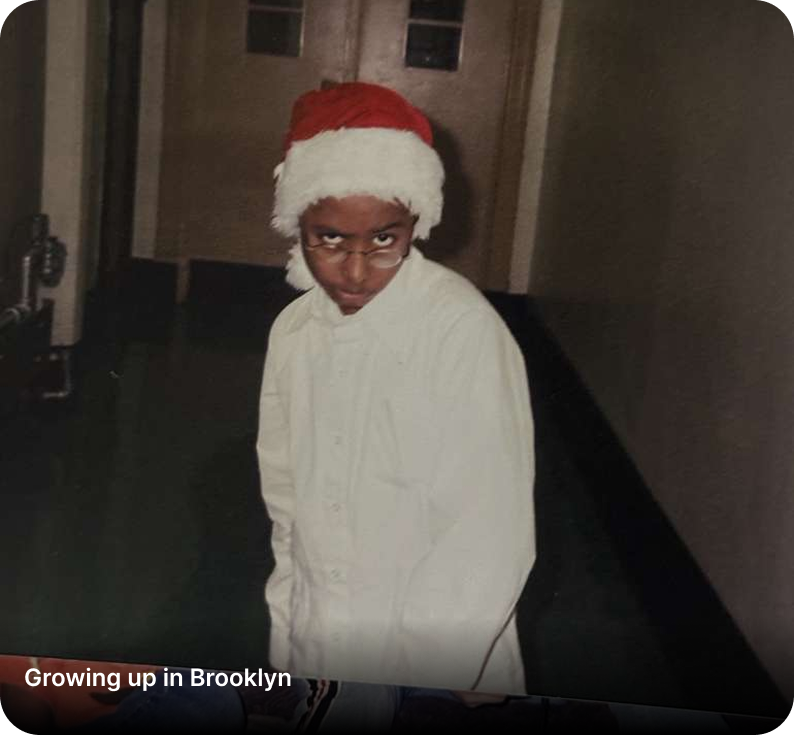 A young person wearing a Santa hat, glasses, a white shirt, standing indoors with a serious expression.