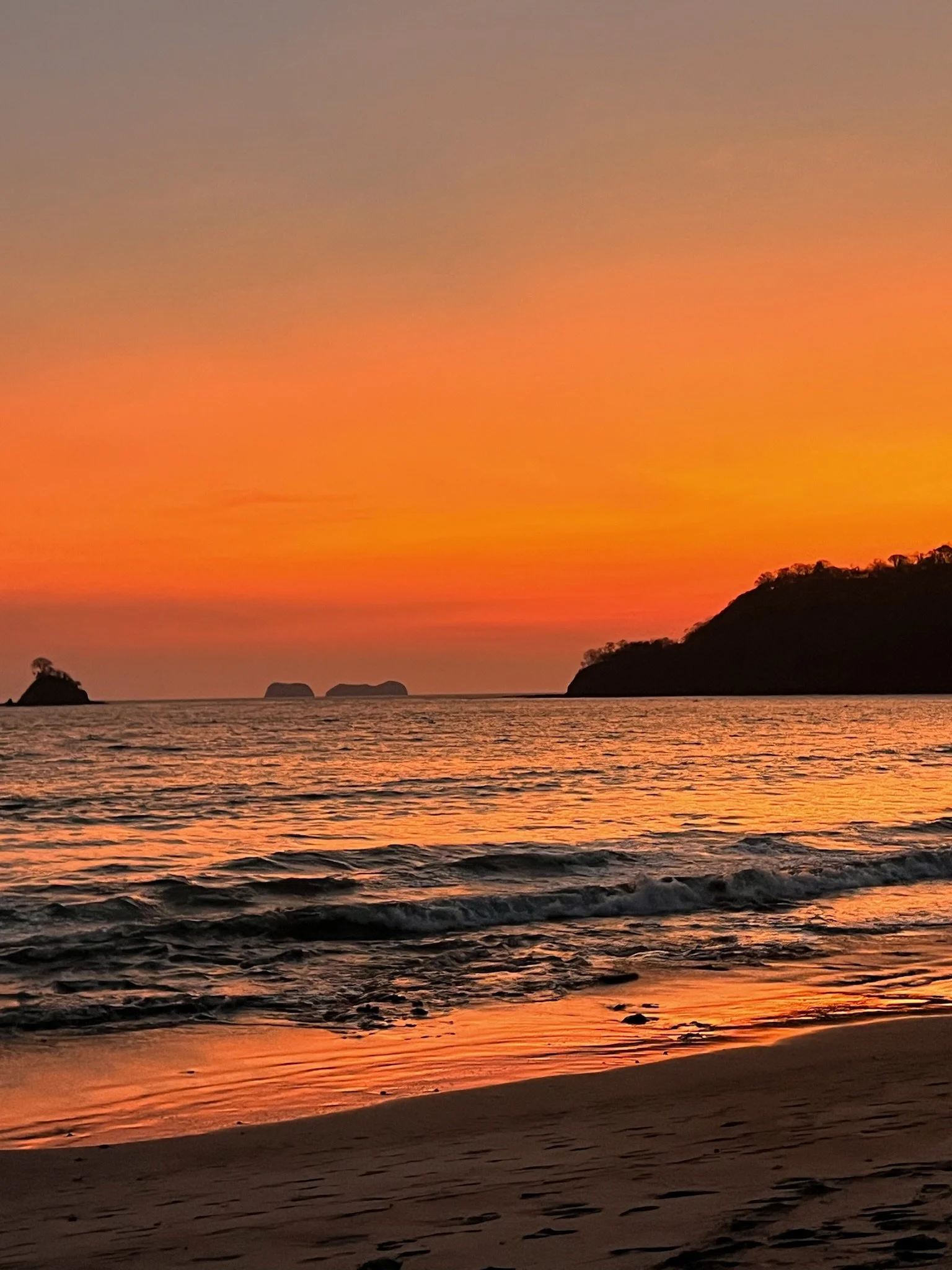Beautiful sunset over the ocean with orange and pink hues, small islands in the distance, and a sandy beach in the foreground.