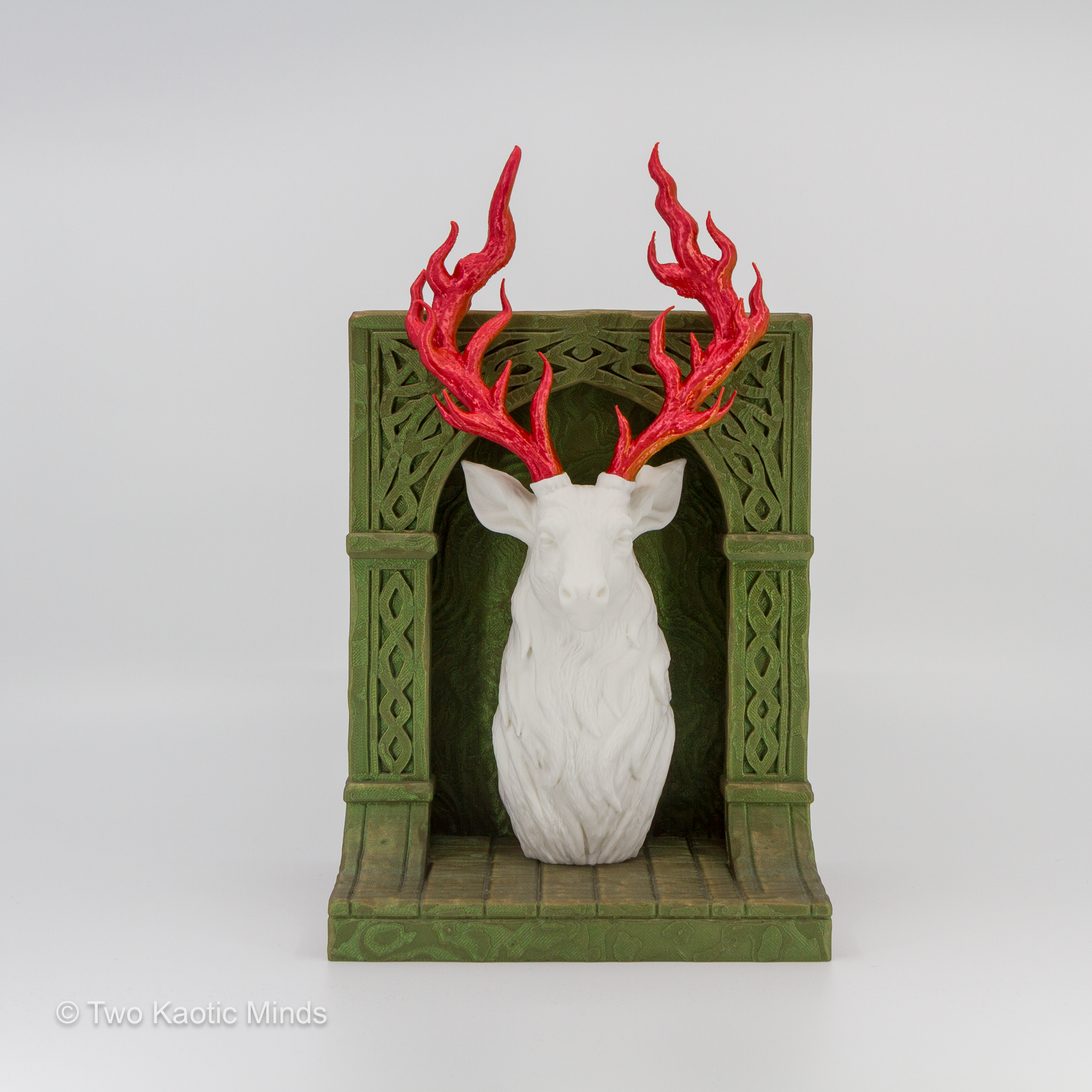 3D printed Throne of Glass inspired white stag book nook with flame gradient antlers in Silk Sunset PLA, framed by an ornately carved Starlight Aurora iridescent green arch on a brown base, front view
