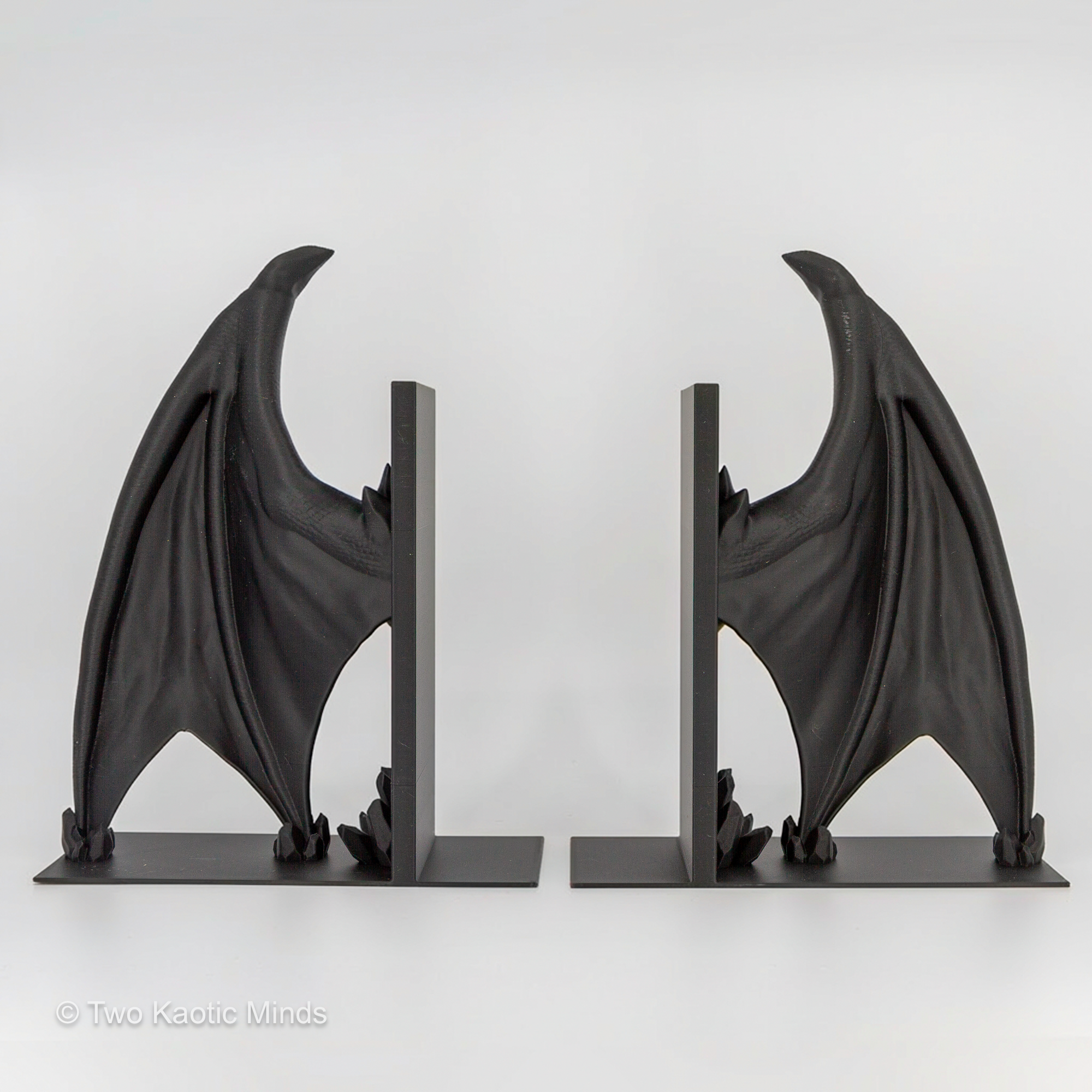 3D printed matte black Frost Dragon wing bookends shown as a pair without books, both dragon wings spread wide on white background, front view