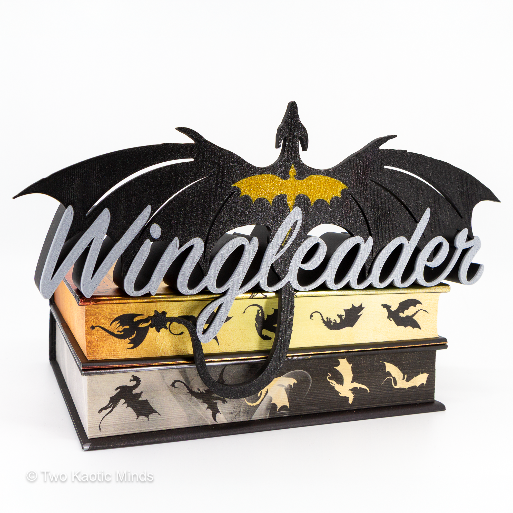 Front view of the Fourth Wing inspired Wingleader shelf sign showing the Wingleader script and dragon with wings spread, displayed resting on a stack of books with tail draped over the edge