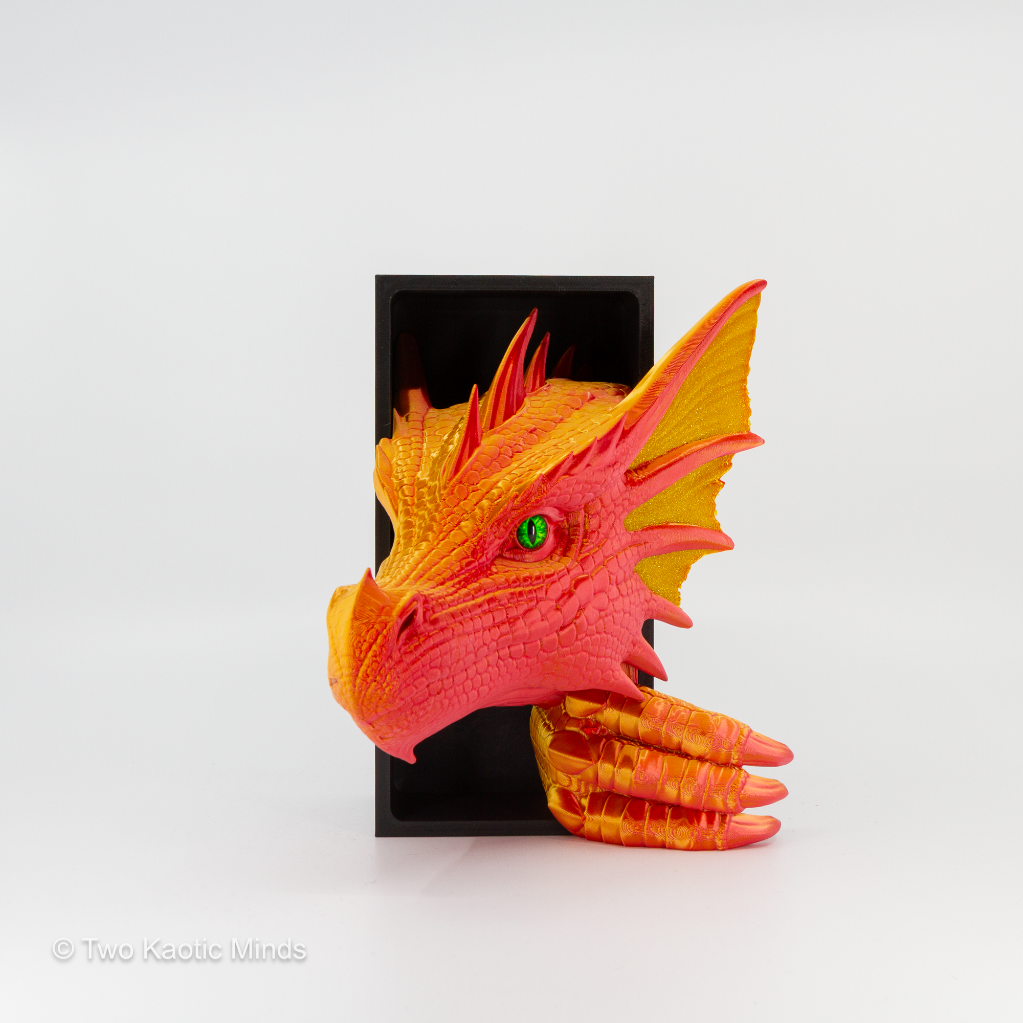 3D printed Sea Dragon book nook in warm red-orange with opaque gold accent fins and green glass eyes, emerging from matte black box, front angle view