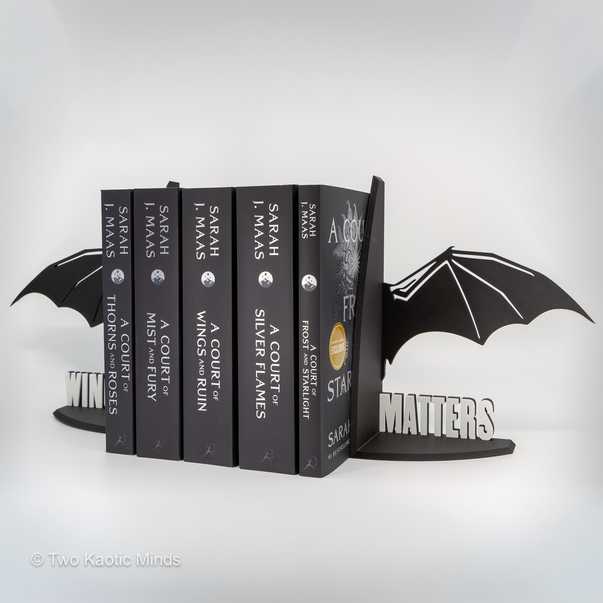 Low front angle view of the Wingspan Matters dragon bookends with a full row of fantasy books between them showing the dramatic wing height