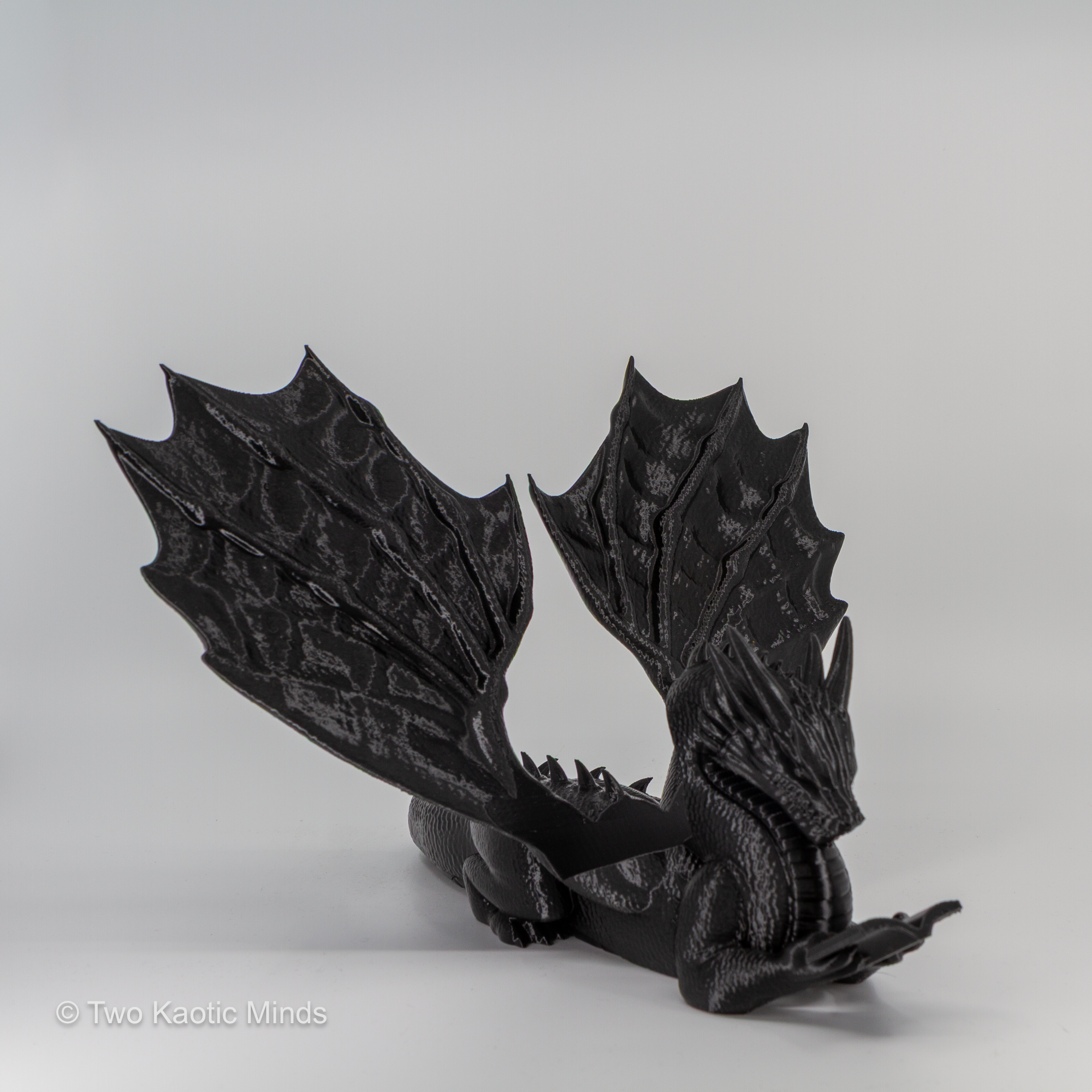 3D printed black dragon book holder with wings spread wide, front view on grey background, no book