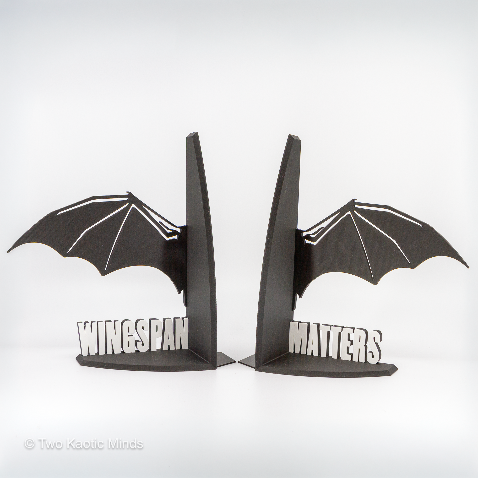 Pair of 3D printed black dragon wing bookends with white WINGSPAN and MATTERS lettering, shown together without books on white background, front view
