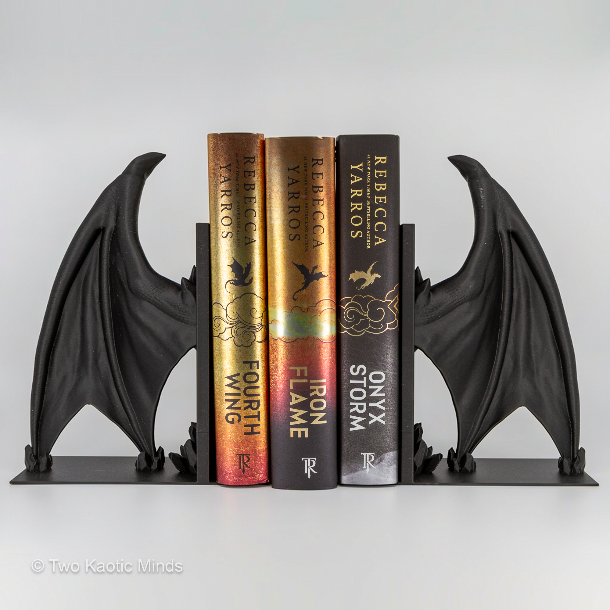 Frost Dragon wing bookends in use holding a row of fantasy books between them, front view showing full wing spread flanking the book spines