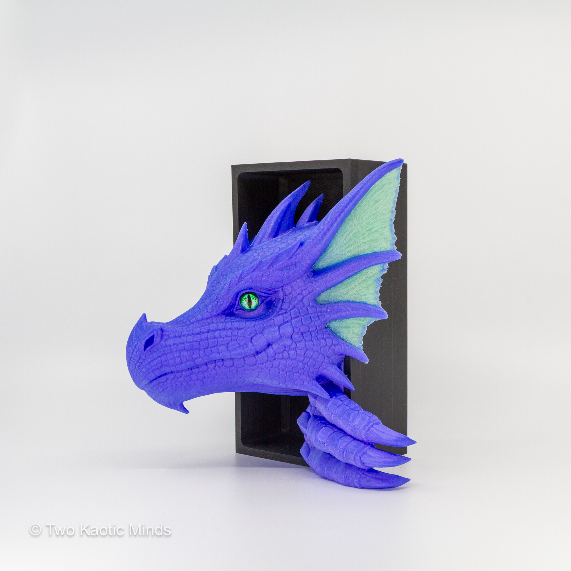 3D printed Sea Dragon book nook in vibrant purple with translucent jade green accent fins and green glass eyes, emerging from matte black box, front angle view