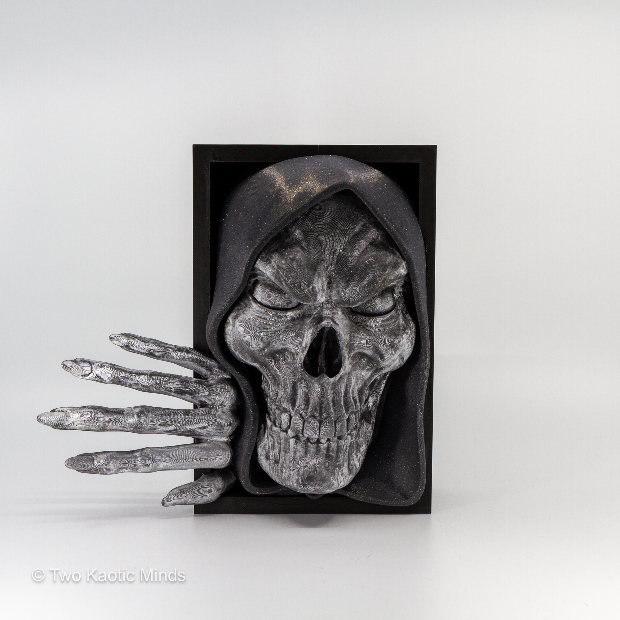 3D printed Bone Keeper book nook showing a pewter silver skull with skeletal hand emerging from a matte black box, front angle view on grey background