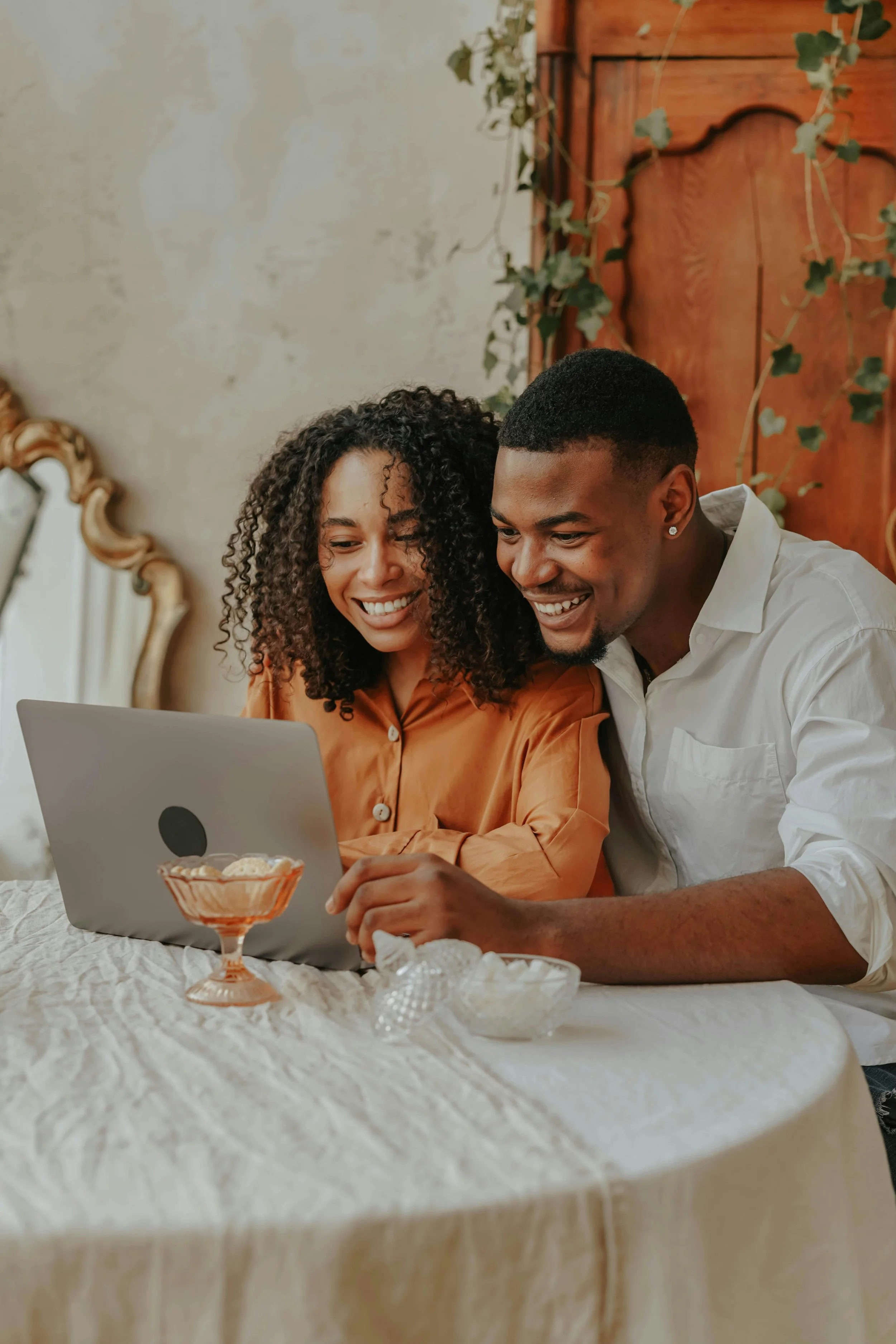 A smiling couple sitting together and looking at a laptop during an online couples therapy session with Kristin Crumbley, LMHC, LMFT.