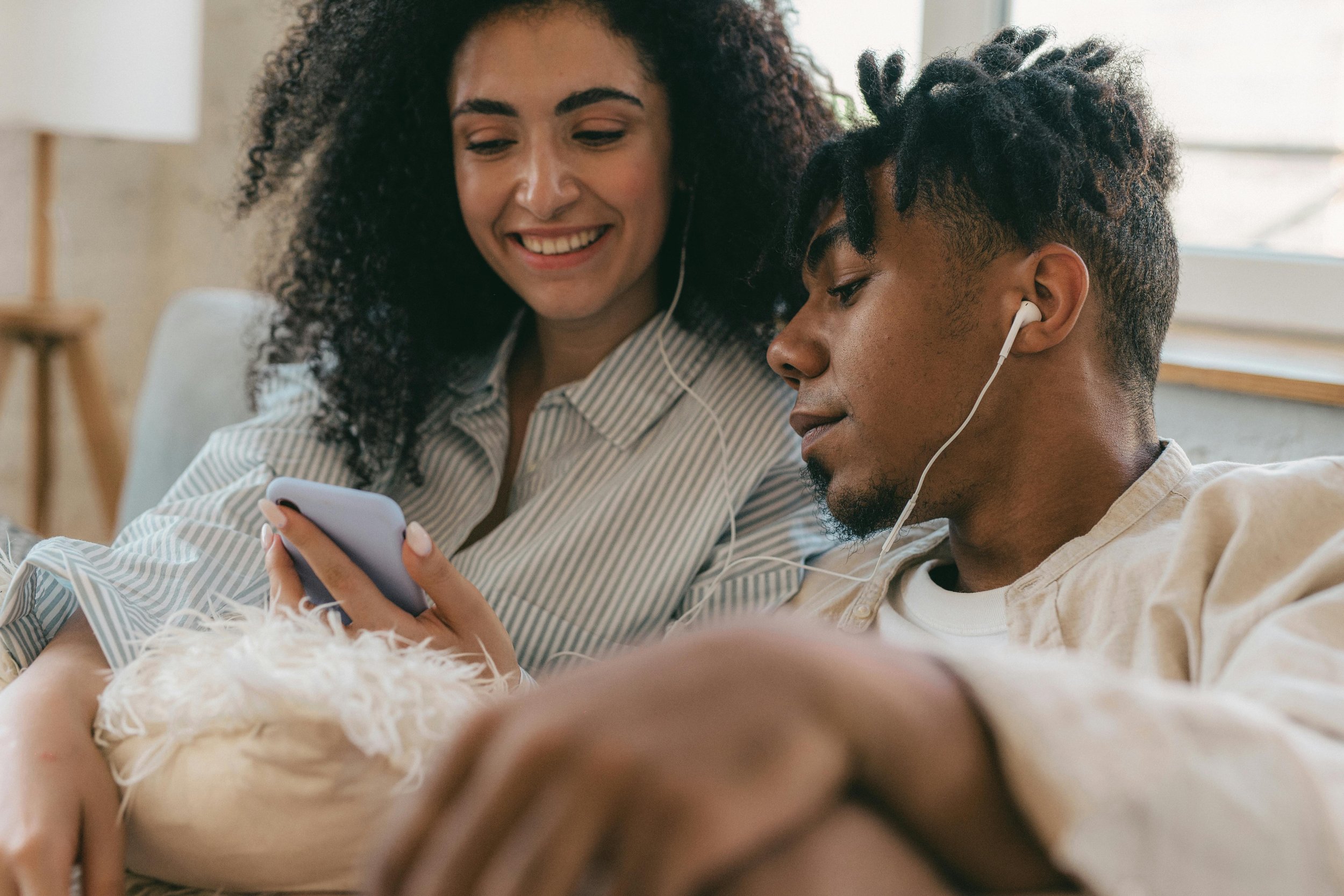 A couple sitting together on a couch, sharing headphones and smiling as they reconnect
