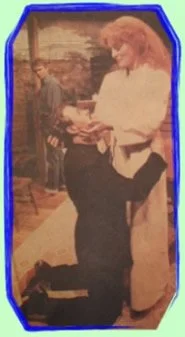 Two women in a cafe, one is seated and the other is standing, engaged in a conversation.