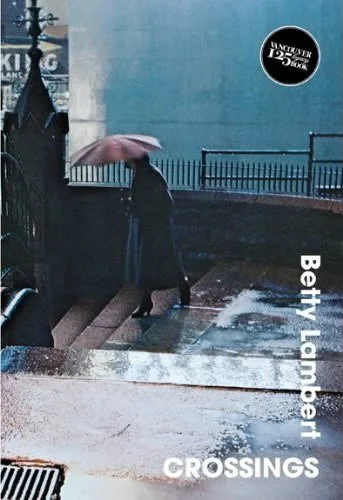 A woman with an umbrella walking down wet stairs outside, with a black fence and blue wall in the background.