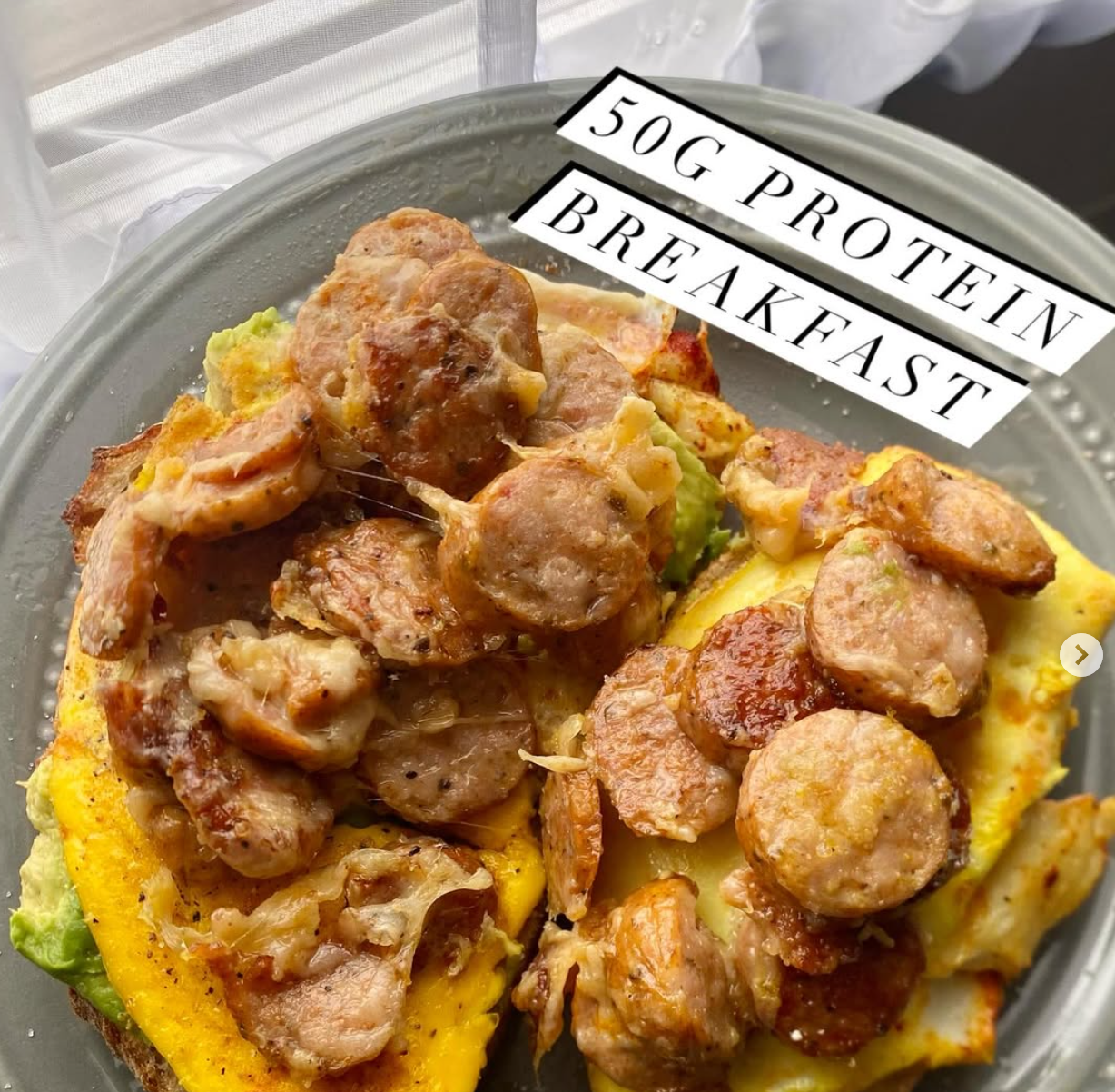 Close-up of a breakfast dish with two omelettes topped with sausage slices, on a grey plate, with a label reading '50G PROTEIN BREAKFAST'