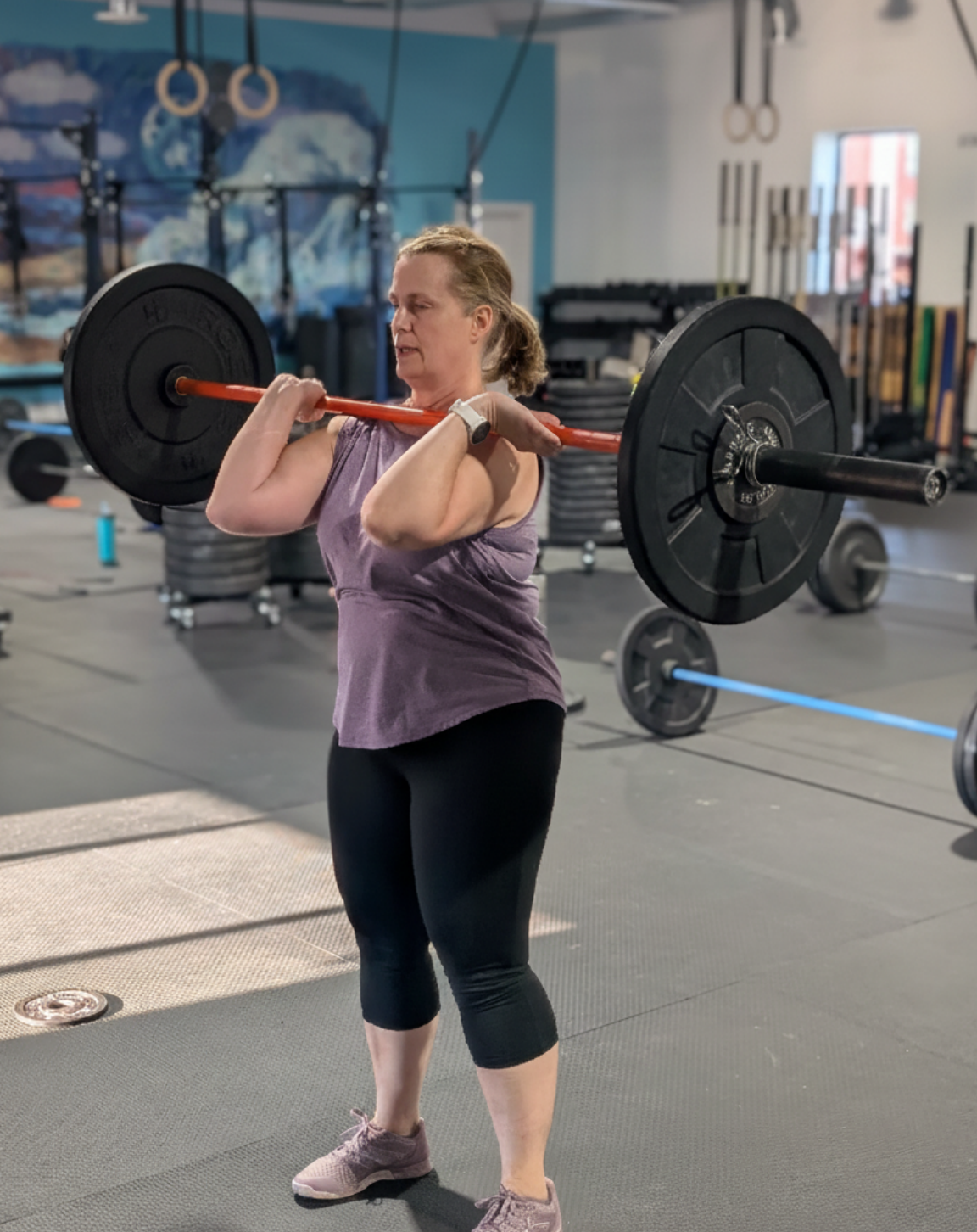A woman lifting a barbell with weights at a gym.