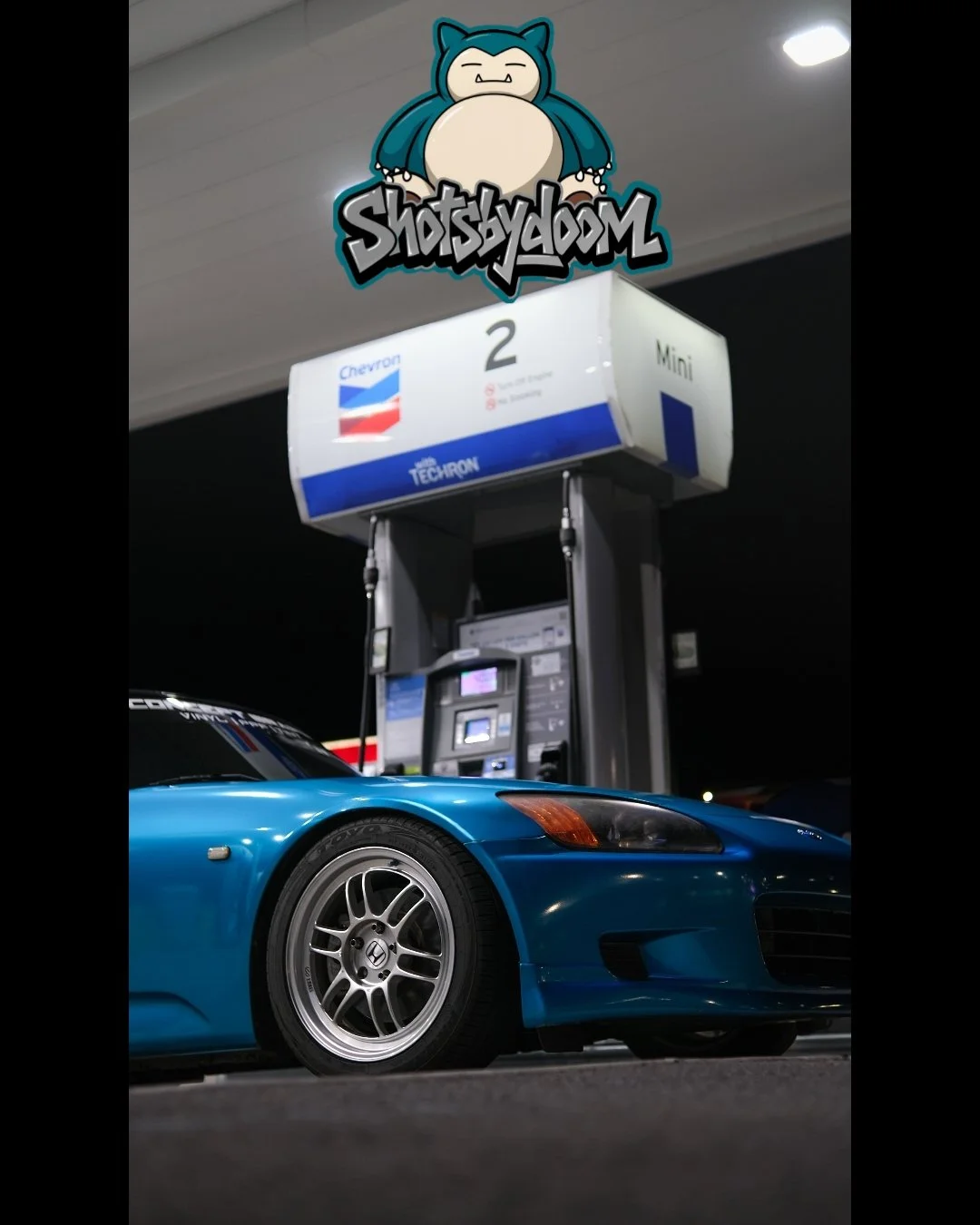 Blue sports car parked at a Chevron gas station pump with a night sky background and a digital payment terminal