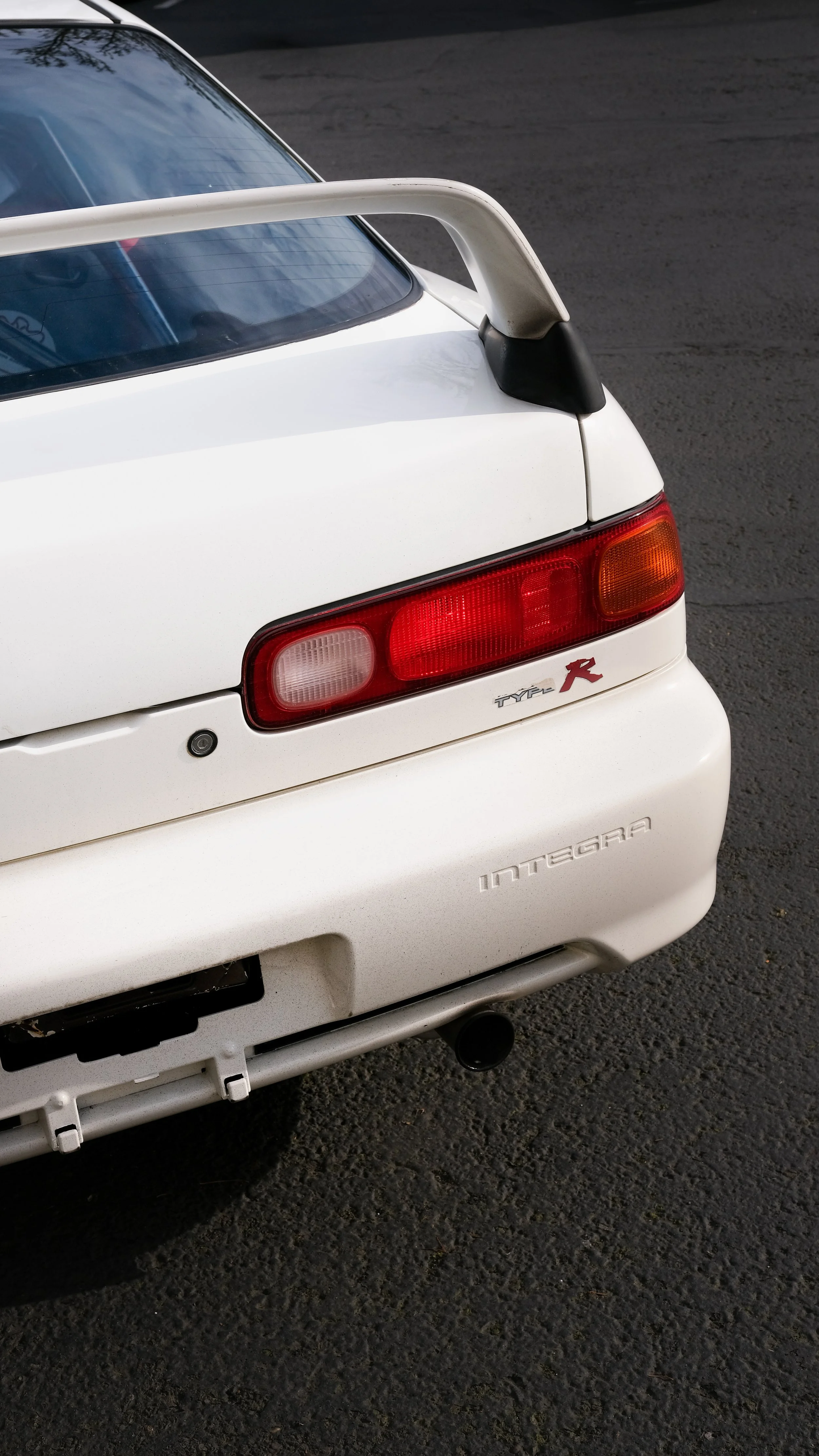 Close-up of the rear end of a white Nissan Skyline GT-R R32, showing taillights, rear spoiler, and model badges.