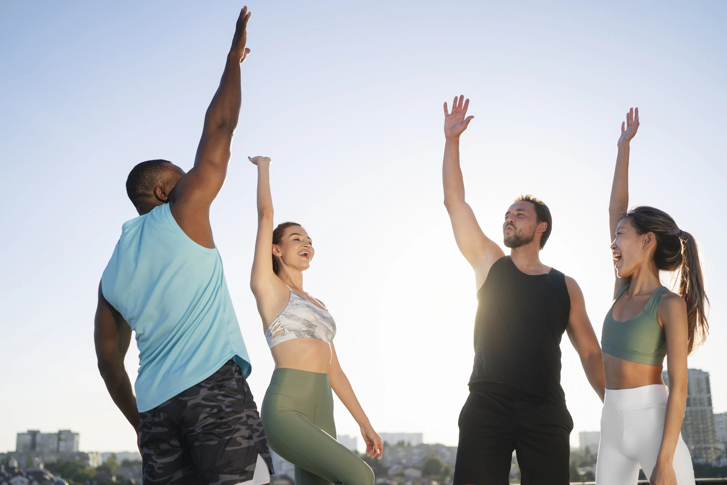 Four people exercising outdoors, raising their arms in the air, with a city skyline in the background.