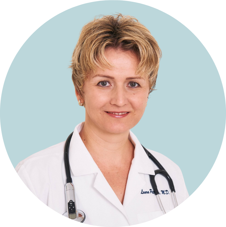 A female doctor with short blonde hair wearing a white coat and a stethoscope around her neck, smiling at the camera against a light blue background.