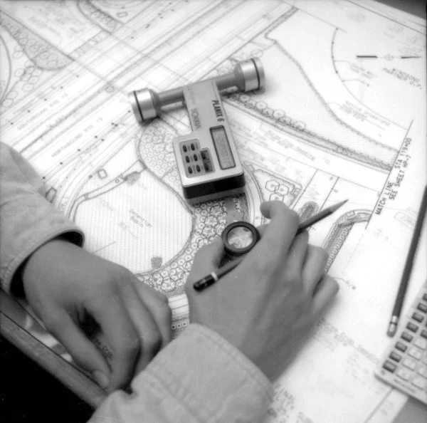 A team member working on an architectural plan, using a magnifying glass and a pen, with a digital caliper on the table.