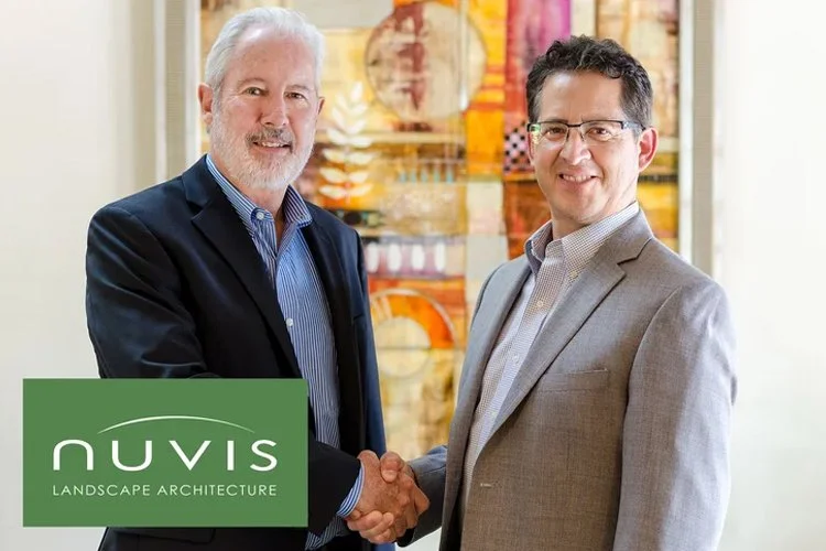 Bob Stone and Perry Cardoza shake hands and smile at the camera in the office, with colorful abstract art in the background. Logo in the lower left corner reads "NUVIS Landscape Architecture."