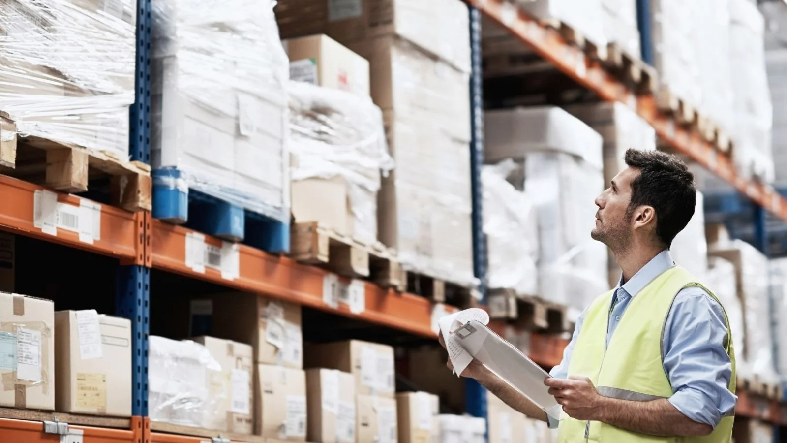 Warehouse manager checking stock records against racked pallets of imported goods in a bonded warehouse