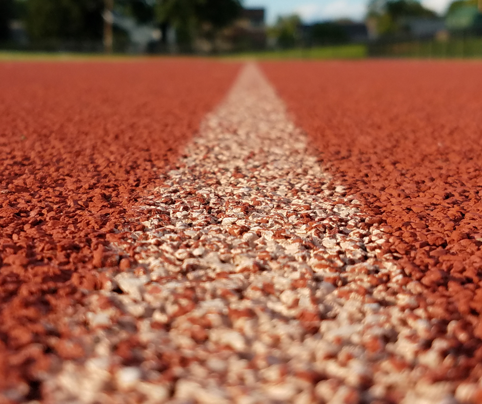 Close-up view of a red running track with a white line in the center, with grass and trees in the background. Image implies the start of a business journey in international trade and mastering HMRC customs regulations.