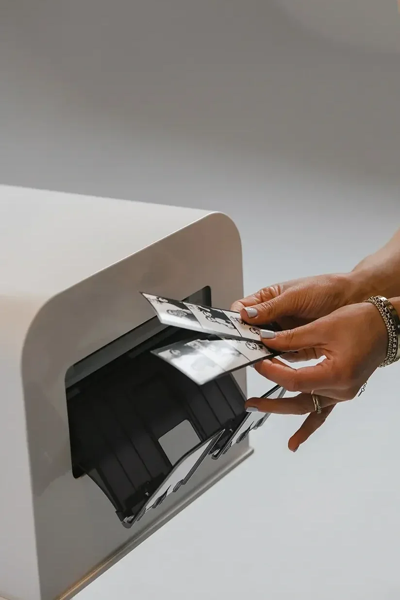 Une personne insère des photos dans une imprimante ou un scanner moderne de couleur blanche sur un fond gris.