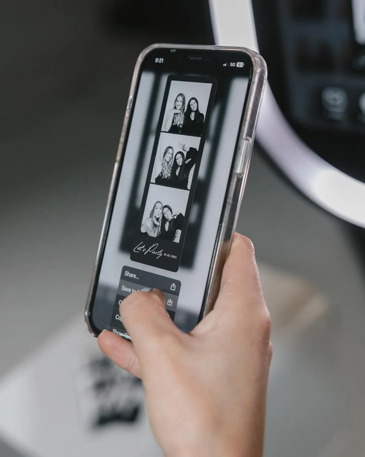 Un téléphone portable affichant une série de photos en noir et blanc de deux femmes qui posent pour une séance photo. La photo montre un montage de plusieurs clichés, avec le texte 'et Part' et une date. L'écran montre également des options de partage et de sauvegarde.