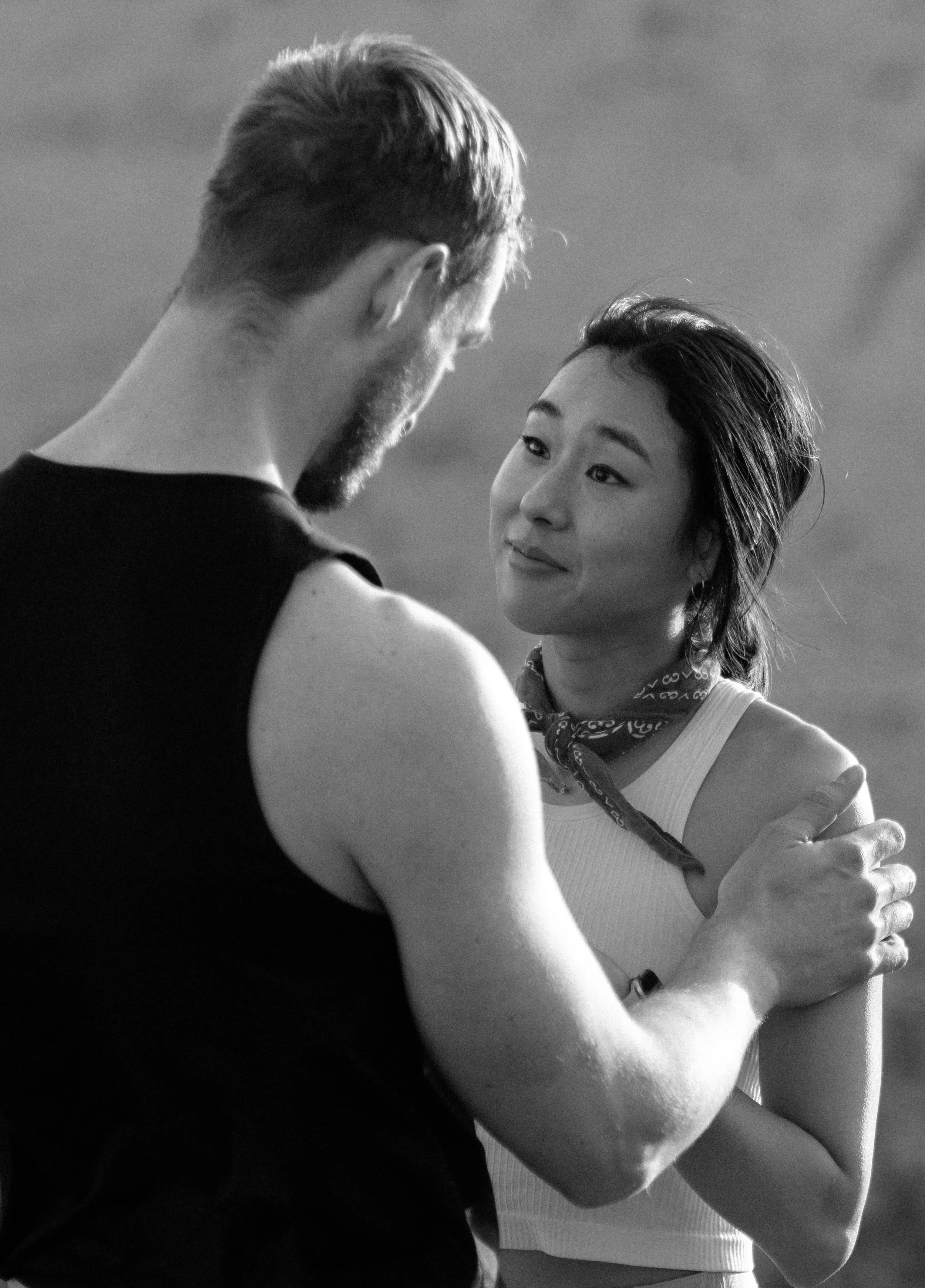 A man and a woman are holding each other and looking into each other's eyes outdoors in a moment of intimacy.