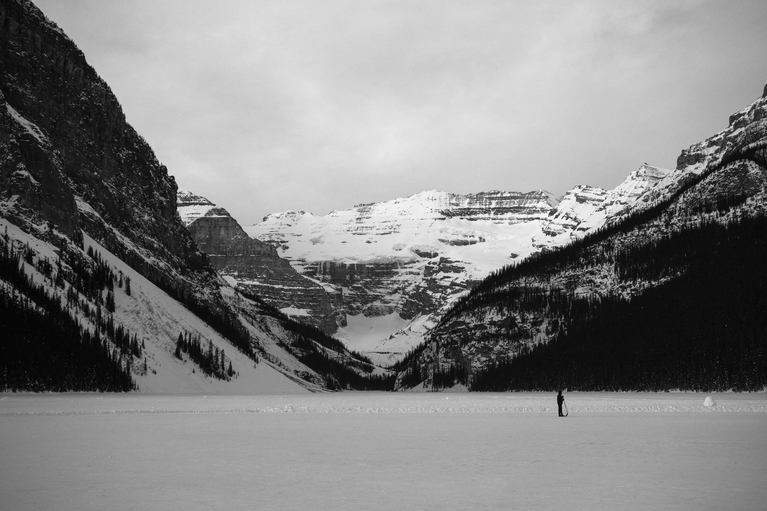 Black and white photo of a snowy mountain landscape with a person standing on the snow in the foreground.