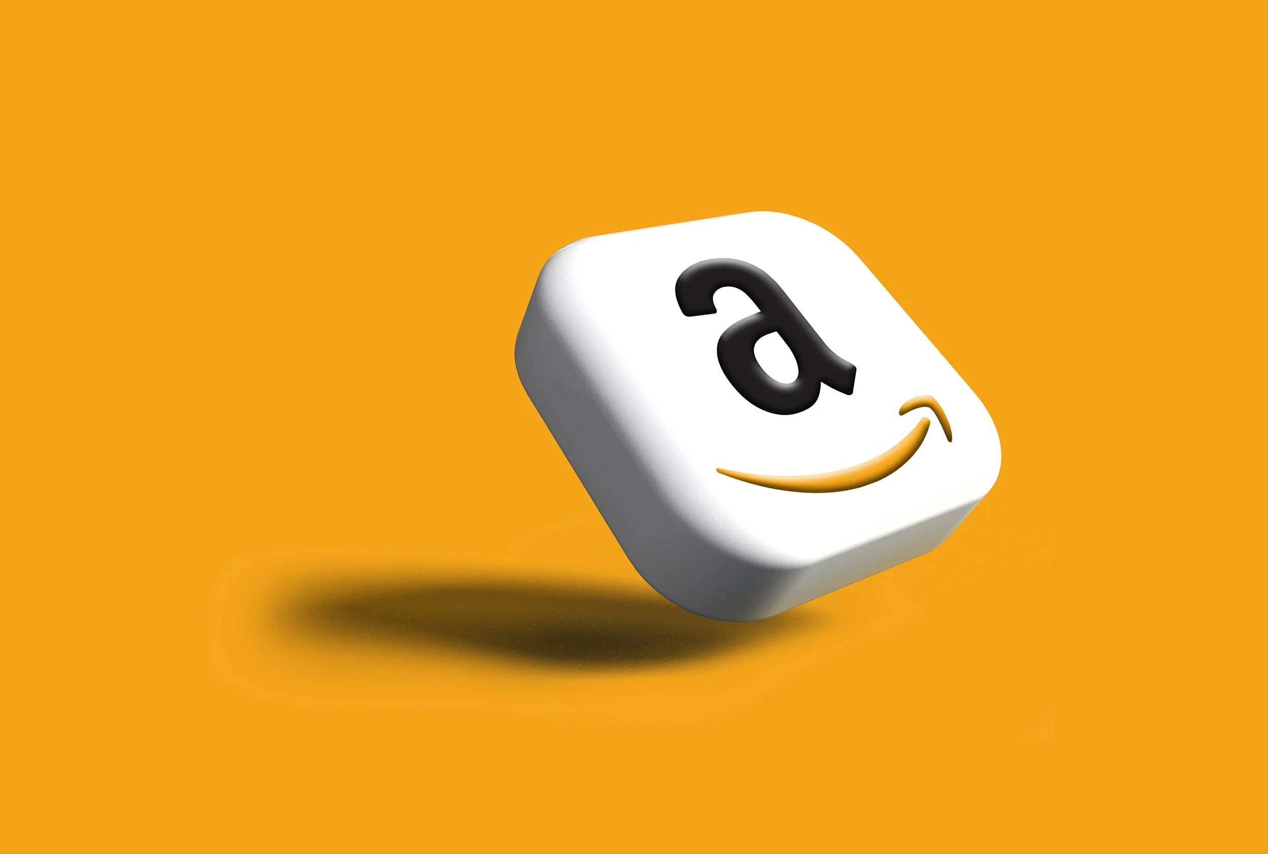 A white cube with an Amazon logo that features a black lowercase 'a' and a yellow arrow forming a smile, floating against an orange background.