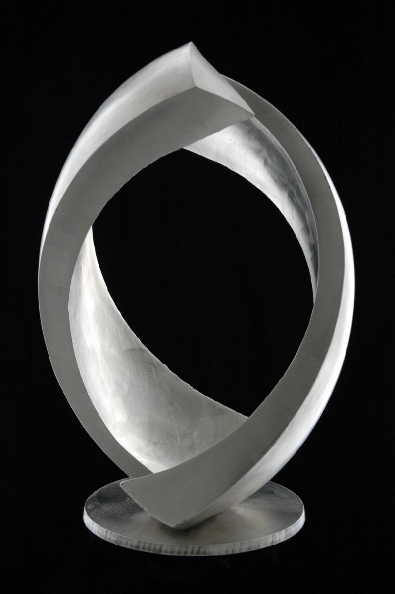 A modern, abstract stainless steel sculpture featuring smooth, compound curves, and overlapping shapes set against a black background.