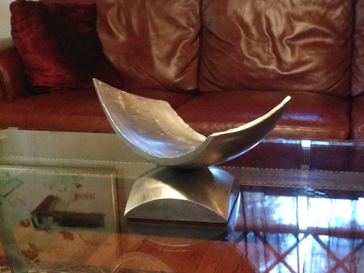 A stainless steel  sculpture on a glass top table, with a leather couch in the background.