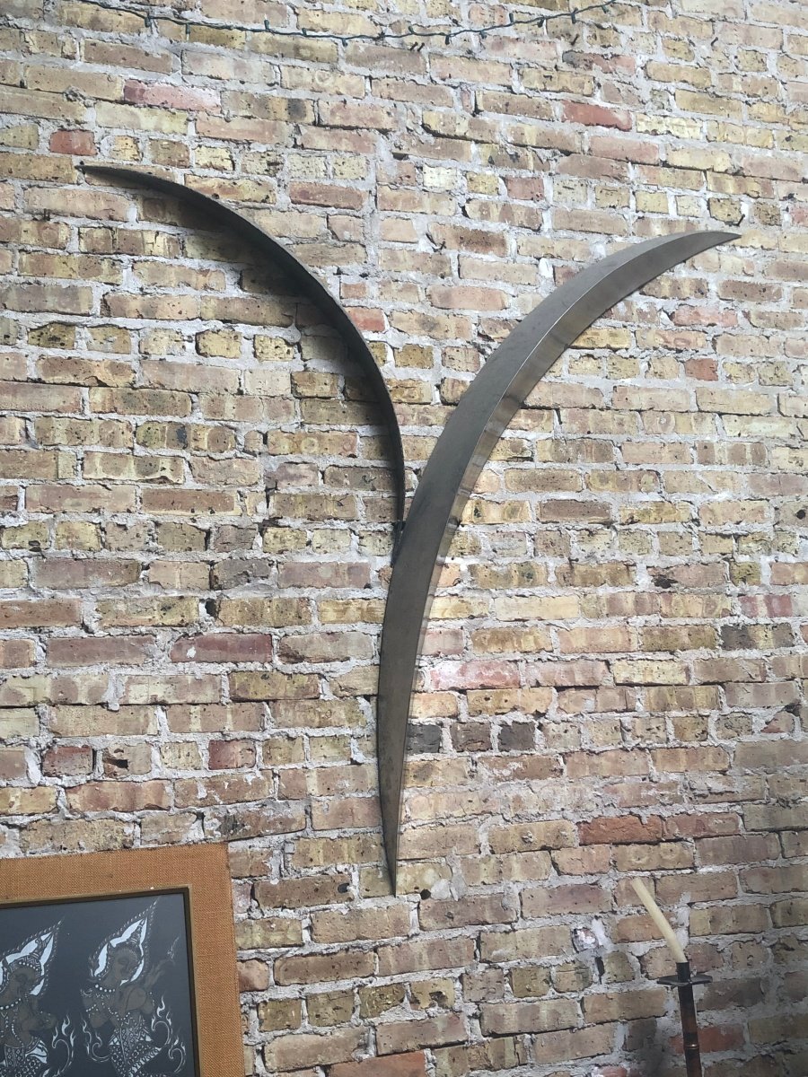 A curved stainless steel sculpture mounted on a brick wall.