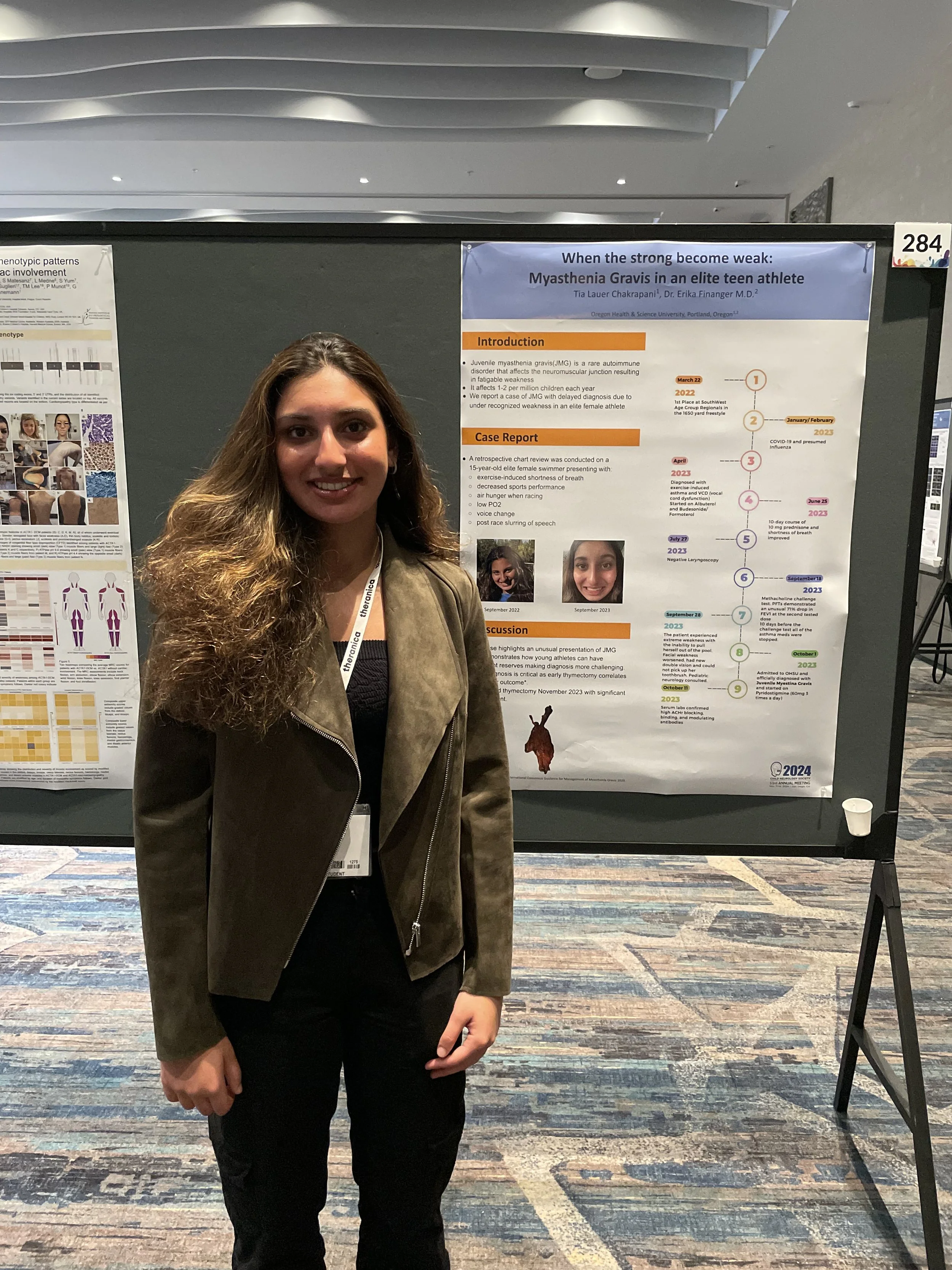 A woman with long curly hair wearing a brown jacket and black outfit standing in front of a research poster at a conference.