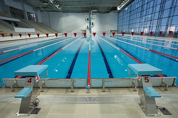 Indoor Olympic-sized swimming pool with lanes numbered 4 and 5, red lane dividers, starting blocks at the near end, and large windows on the right side.