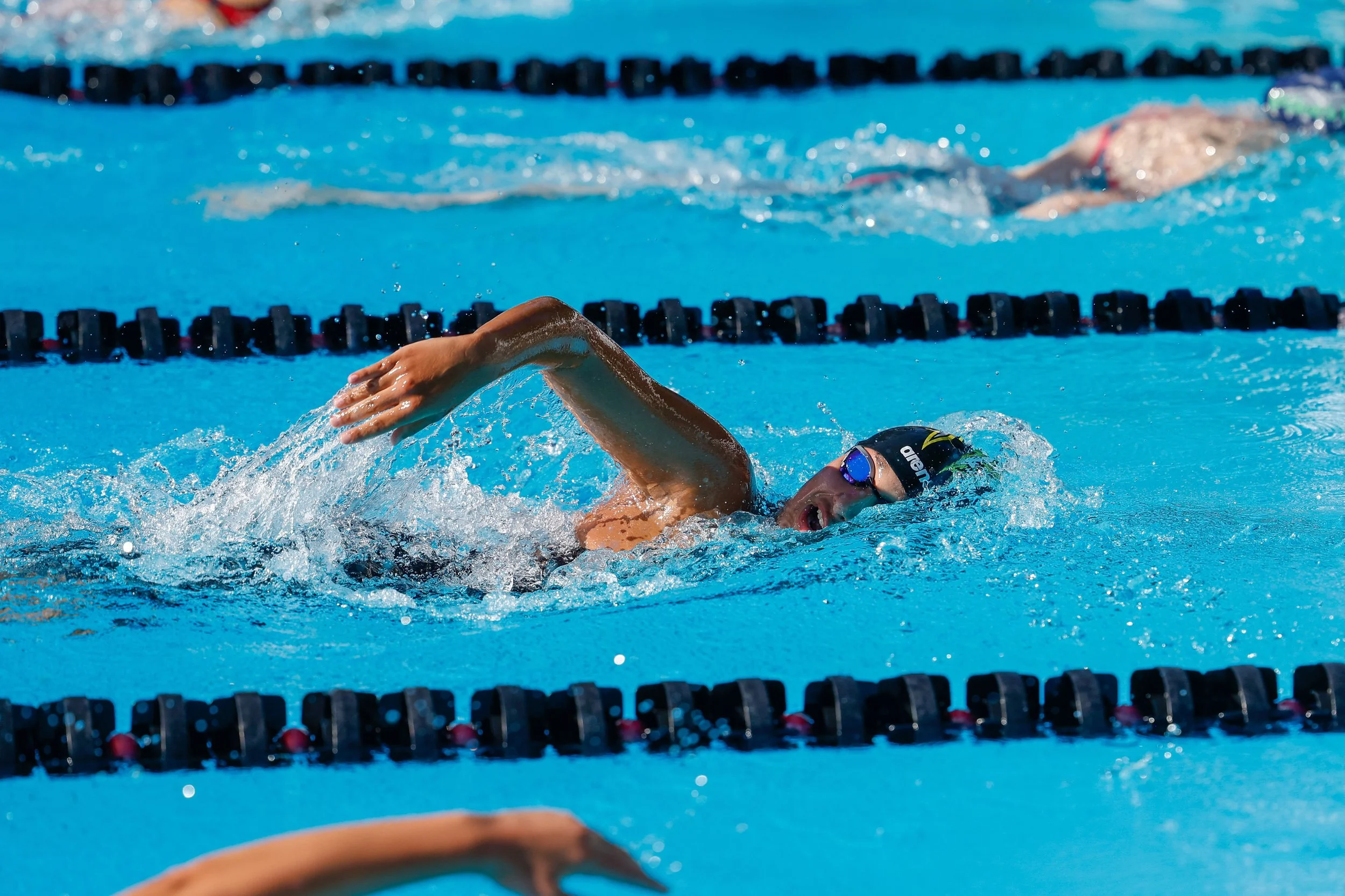 Swimmer in a blue pool wearing goggles and a swim cap, swimming freestyle.