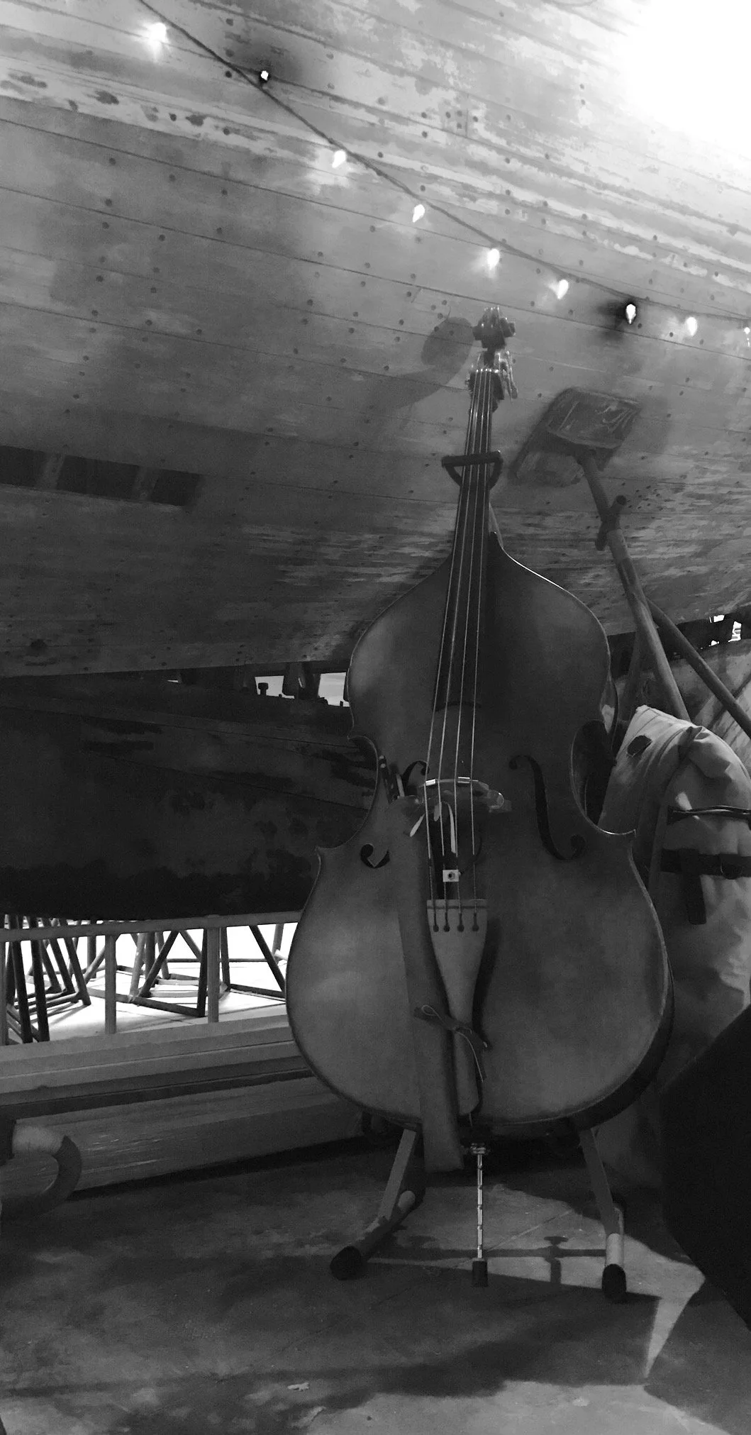 A double bass standing on a music stand with wooden Concordia Sailboat and a string of small lights overhead.