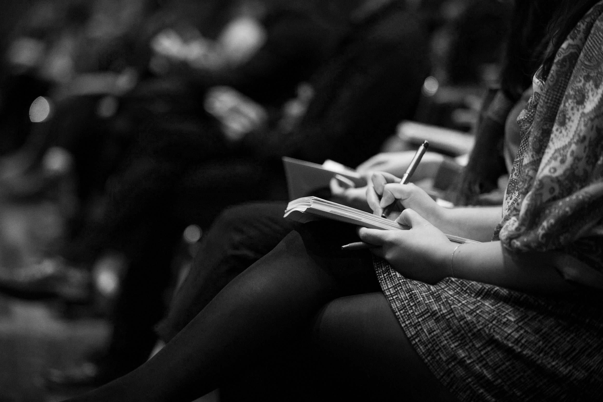 Lou Boyles. The ADHD Coach For Mums. A person taking notes with a pen in a notebook, sitting in an audience or classroom environment.