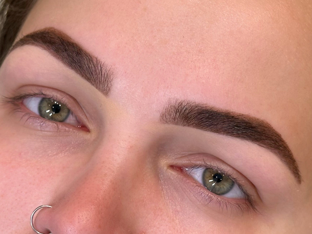 Close-up of a person's face focusing on well-groomed eyebrows, green eyes, and clear skin.