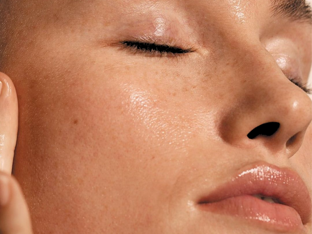 Close-up of a woman's face with smooth, dewy skin, closed eyes, and glossy lips.