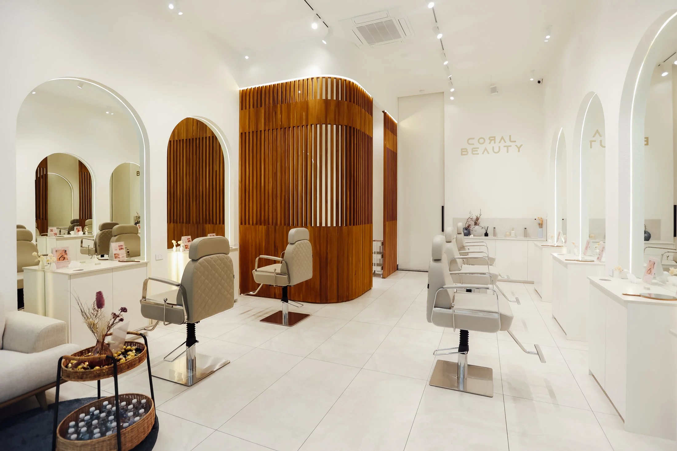 Interior of a modern beauty salon with white walls, arched mirrors, beige chairs, and a wooden accent wall.