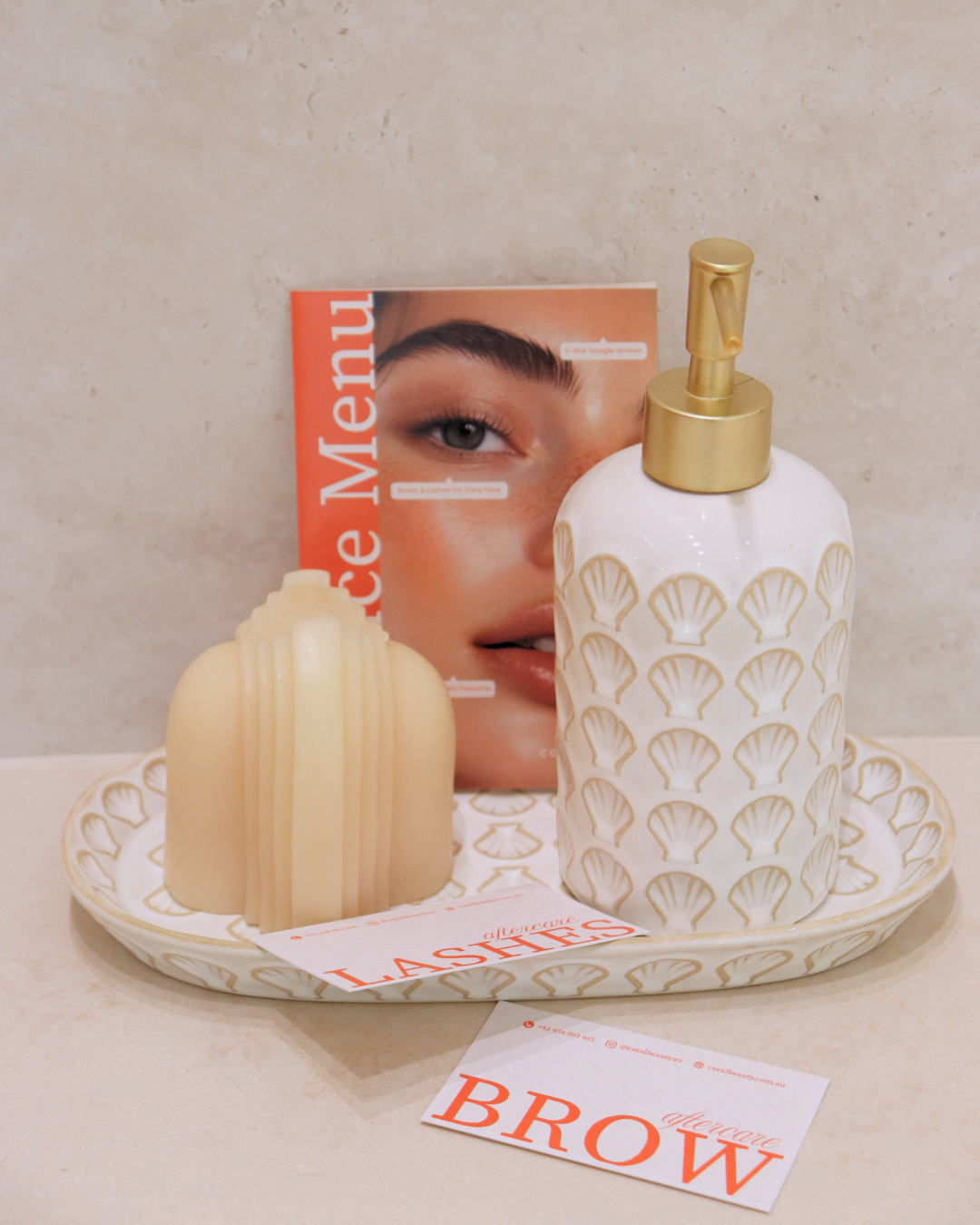 Beauty products on a tray with a magazine and business card, including a decorative soap and a lotion dispenser, with the magazine featuring a close-up of a woman's face.