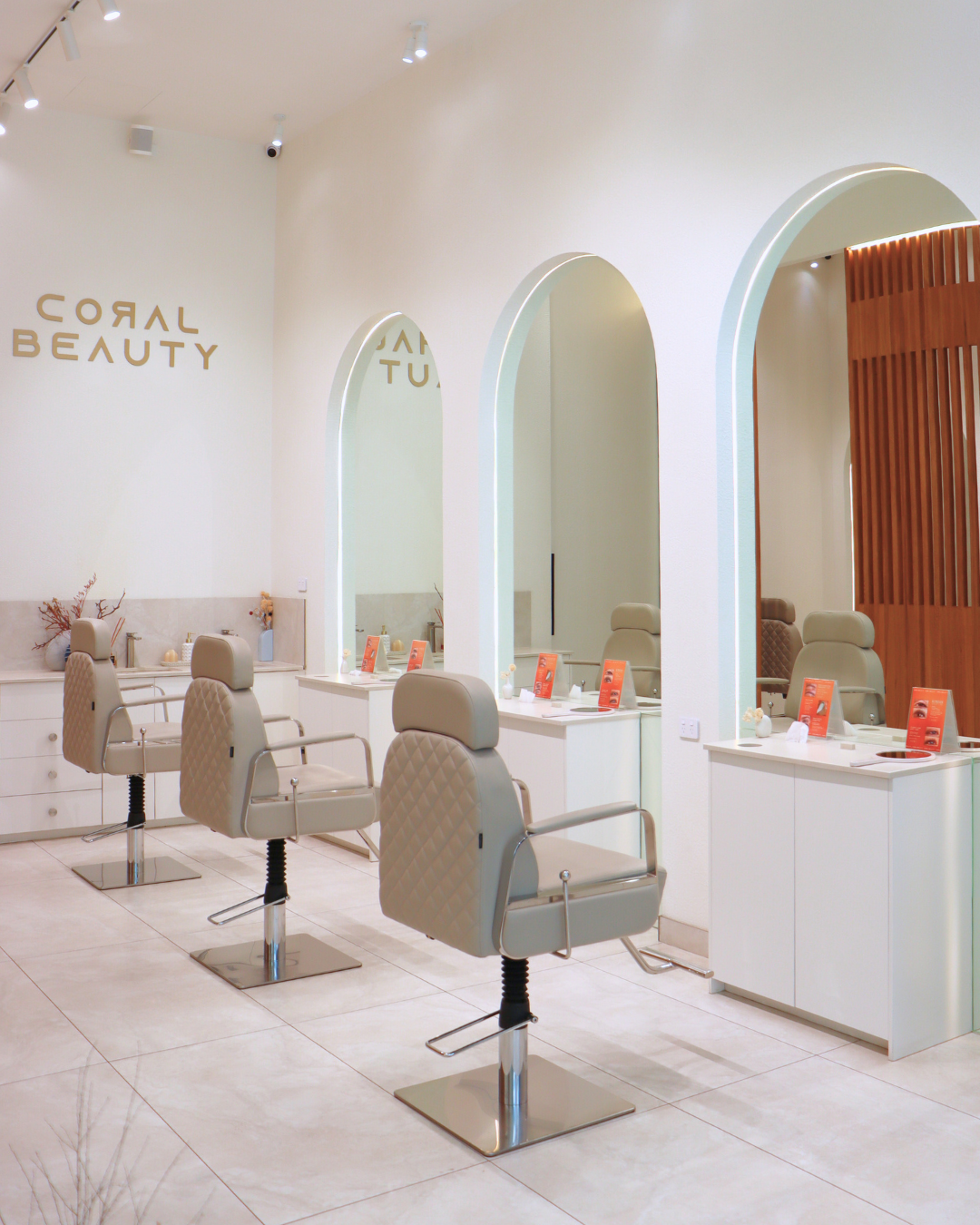 Interior of a beauty salon with three styling chairs and mirrors, decorated in neutral tones.