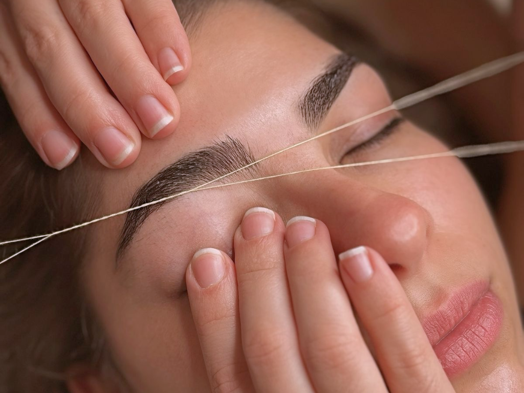 A woman getting an eyelash extension or eyelash grooming treatment, with a professional applying or aligning false eyelashes or natural lash enhancement.