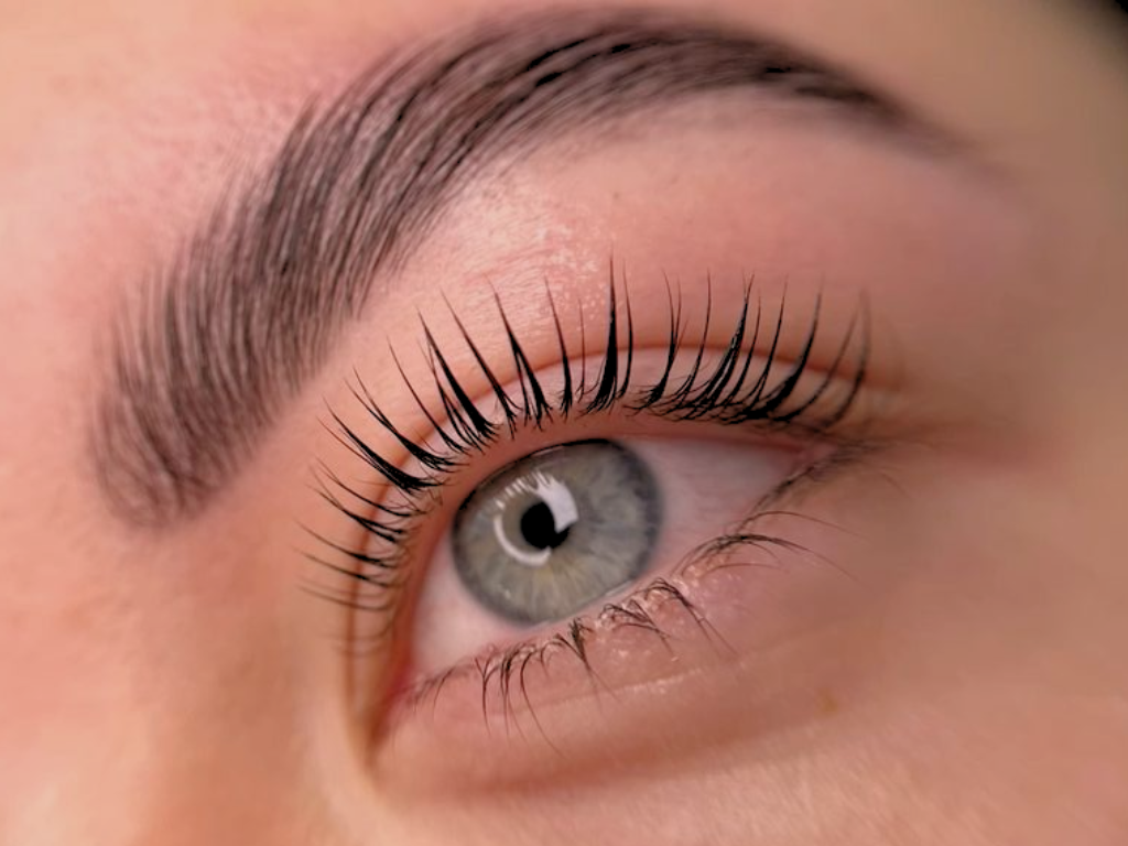 Close-up of a human eye with blue iris, long eyelashes, and well-groomed eyebrow.