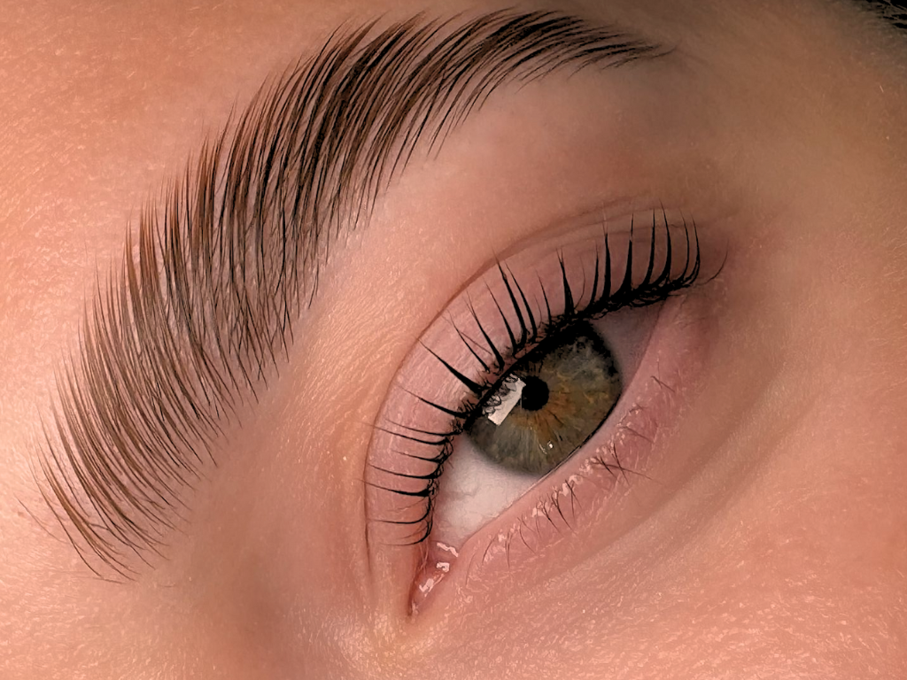 A close-up of a human eye showing detailed eyelashes, eyebrow, and brown iris.